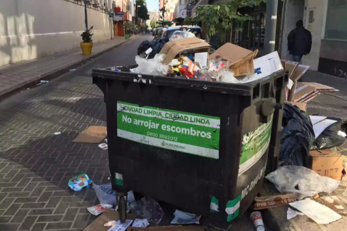 Overflowing trash container with waste and cardboard on an urban street