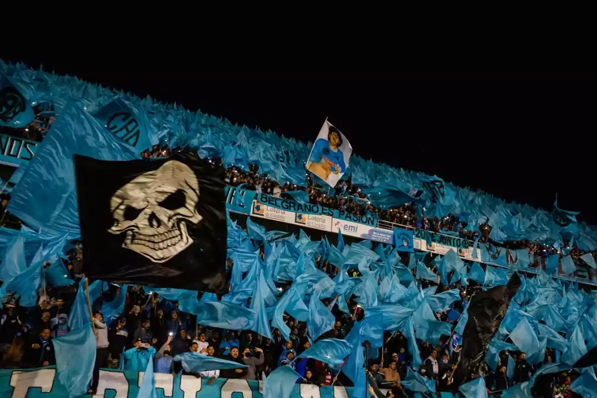 Aficionados en una tribuna ondeando banderas celestes y negras durante un partido de fútbol en un estadio lleno Aficionados en una tribuna ondeando banderas celestes y negras durante un partido de fútbol en un estadio lleno