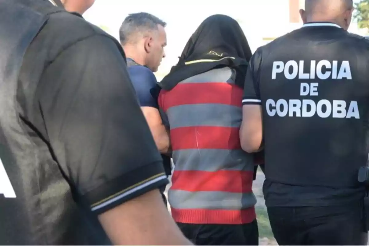 Persona escoltada por policías de Córdoba con la cabeza cubierta y rodeada por agentes Persona escoltada por policías de Córdoba con la cabeza cubierta y rodeada por agentes
