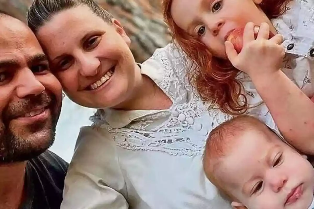A smiling family poses for a selfie while a little girl eats an apple and a baby looks at the camera. A smiling family poses for a selfie while a little girl eats an apple and a baby looks at the camera.