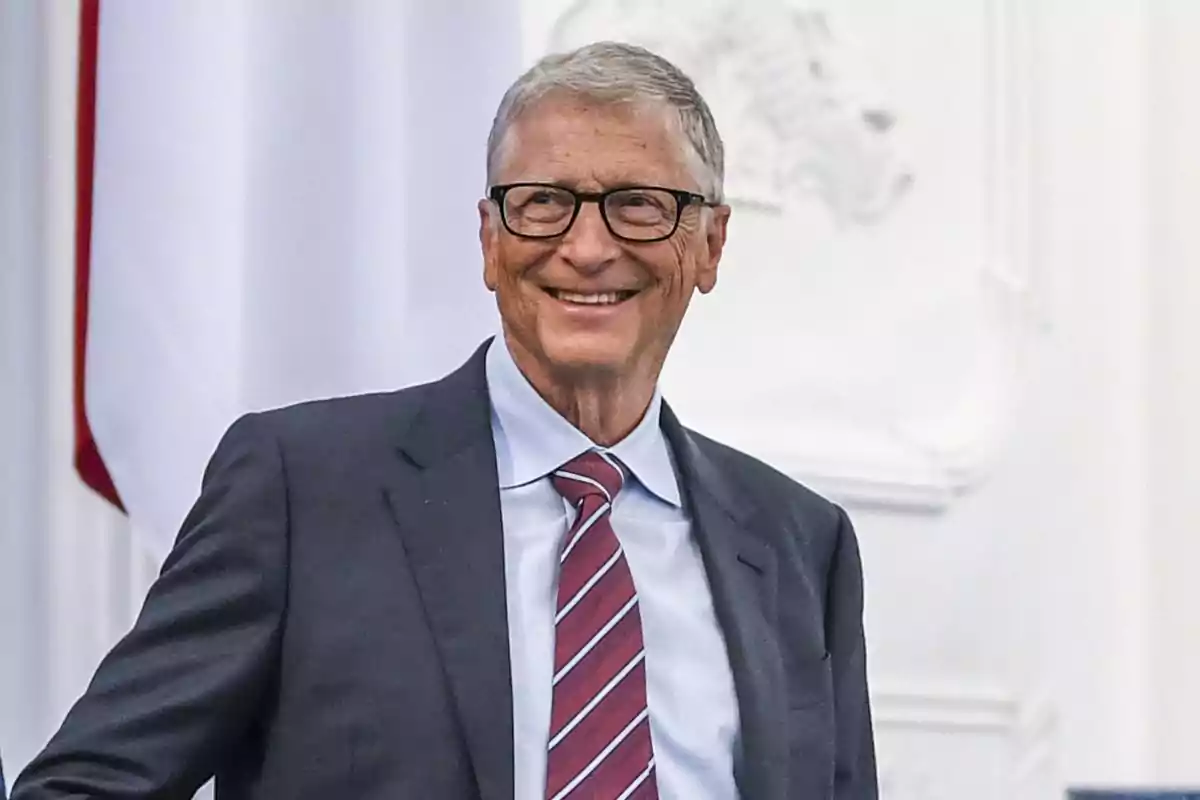 Older man with glasses and a suit smiles in front of a white background