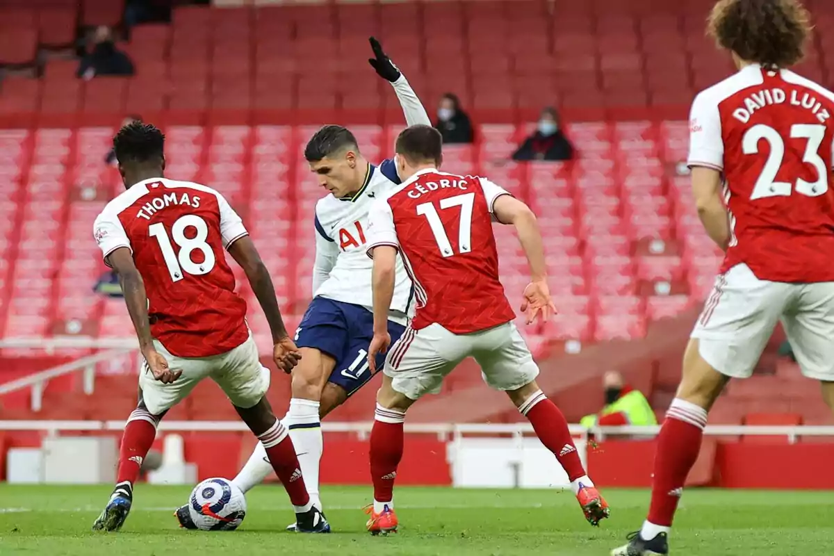 Jugadores de fútbol de los equipos Arsenal y Tottenham disputan el balón en un estadio con gradas vacías. Jugadores de fútbol de los equipos Arsenal y Tottenham disputan el balón en un estadio con gradas vacías.