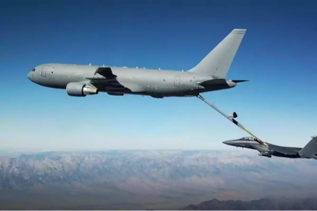 Avión cisterna reabasteciendo a un avión de combate en pleno vuelo sobre una zona montañosa