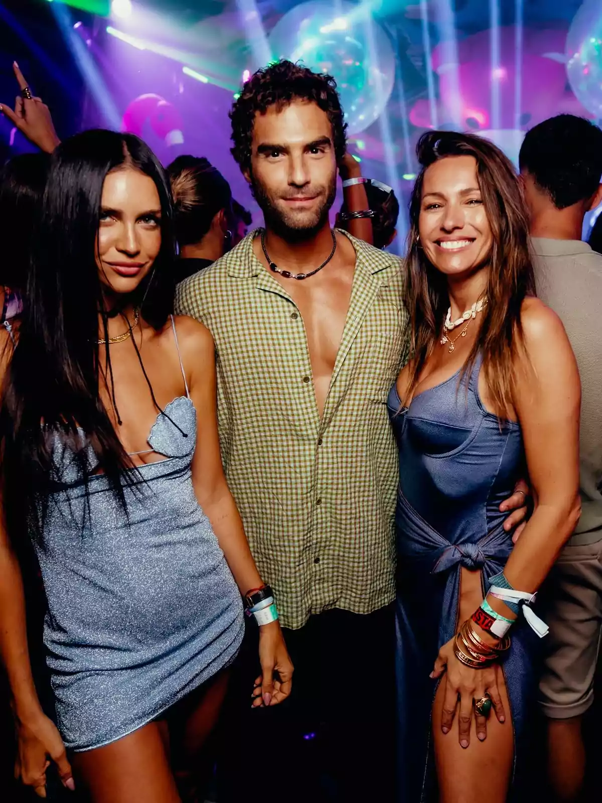 Tres personas posan sonrientes en un club nocturno con luces de colores y ambiente festivo Tres personas posan sonrientes en un club nocturno con luces de colores y ambiente festivo