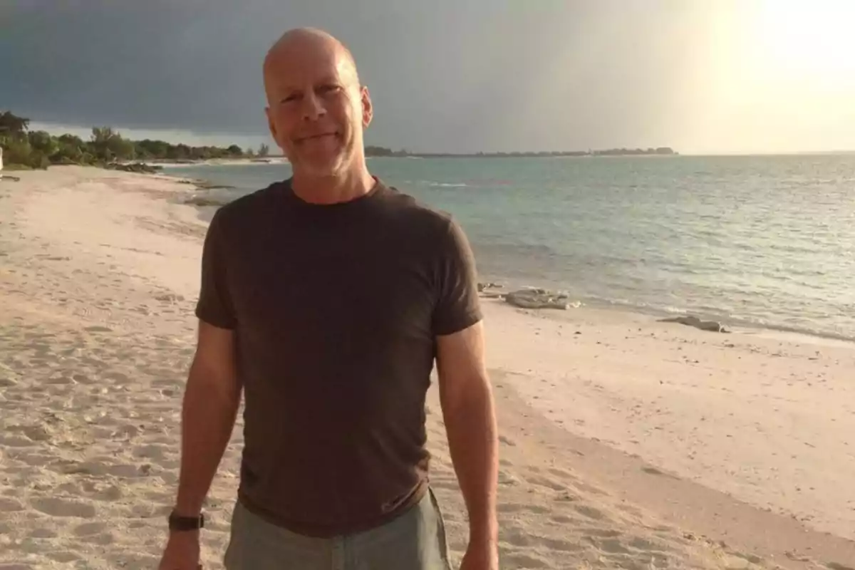 Hombre calvo con camiseta oscura sonriendo en una playa al atardecer con el mar y el cielo nublado de fondo Hombre calvo con camiseta oscura sonriendo en una playa al atardecer con el mar y el cielo nublado de fondo