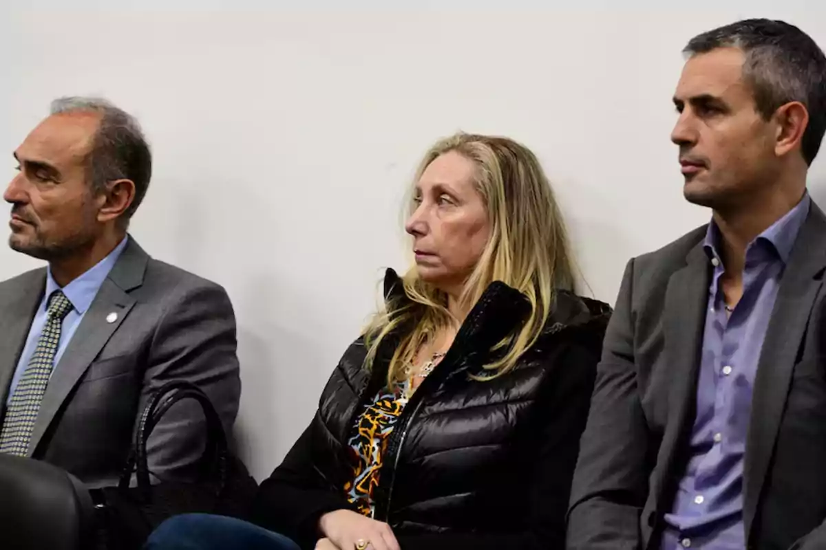 Tres personas sentadas en fila, vestidas de manera formal, mirando hacia el mismo lado con expresiones serias. Tres personas sentadas en fila, vestidas de manera formal, mirando hacia el mismo lado con expresiones serias.
