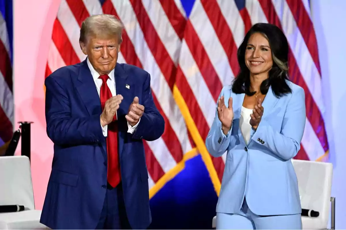 Two people standing and applauding in front of several United States flags
