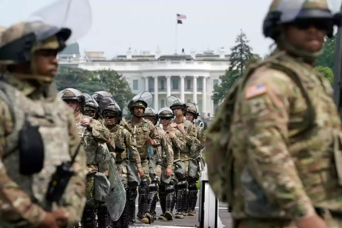 Soldados con equipo antimotines forman una fila frente a la Casa Blanca mientras dos militares están desenfocados en primer plano