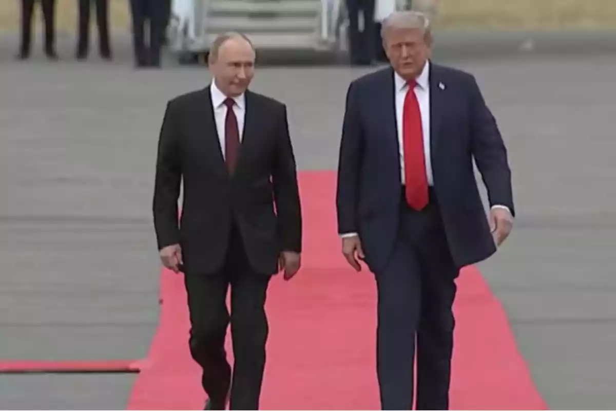 Dos hombres con traje caminando juntos sobre una alfombra roja en una pista de aeropuerto