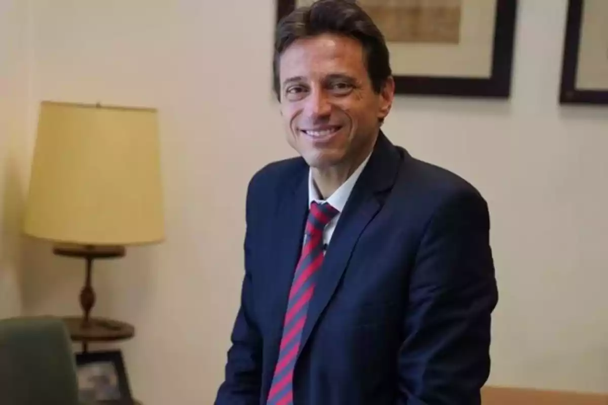 Man in a blue suit and red tie smiling in an office with a lamp and pictures on the wall Man in a blue suit and red tie smiling in an office with a lamp and pictures on the wall
