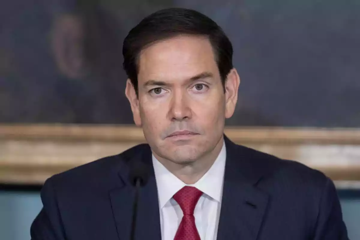Hombre de cabello oscuro con traje azul y corbata roja mirando al frente con expresión seria