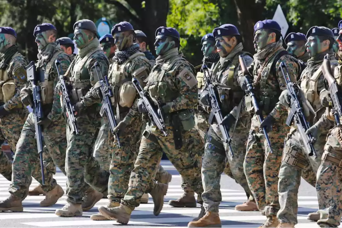 Soldados con uniforme de camuflaje y la cara pintada marchando en formación armados con rifles