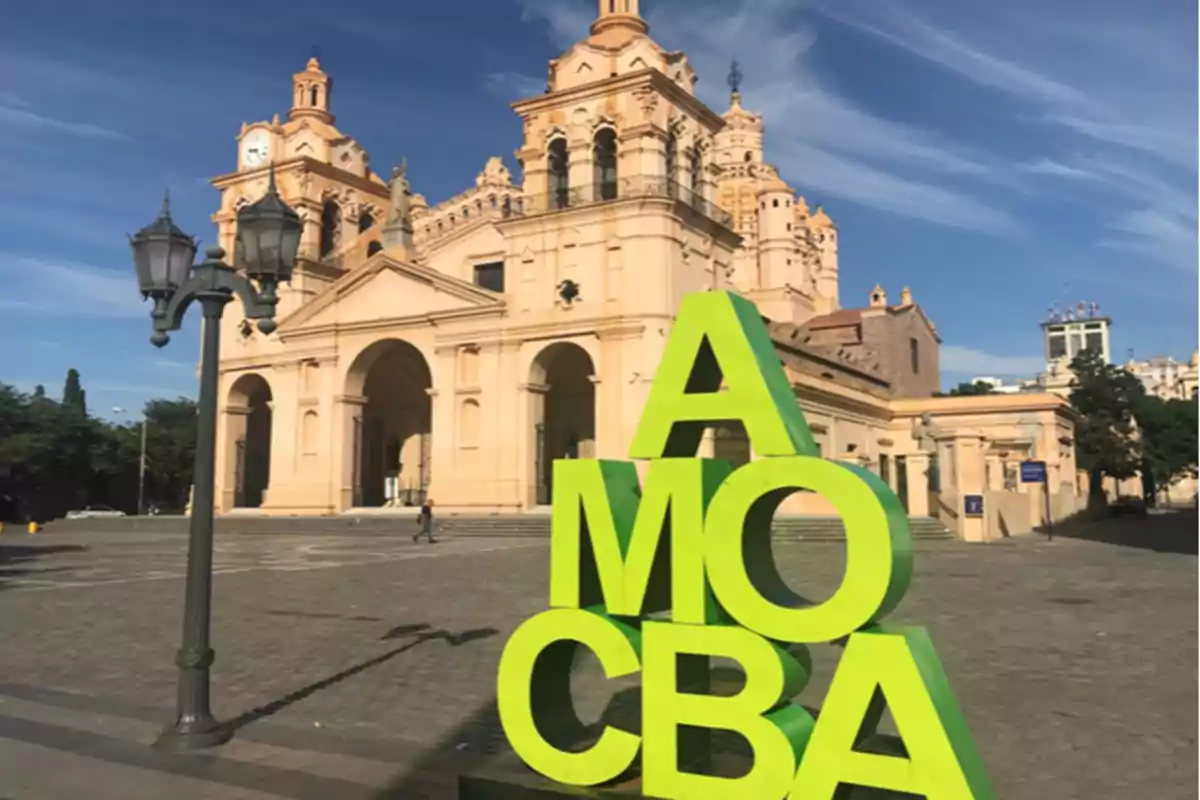 Escultura verde con las letras AMO CBA frente a la Catedral de Córdoba en una plaza bajo un cielo azul