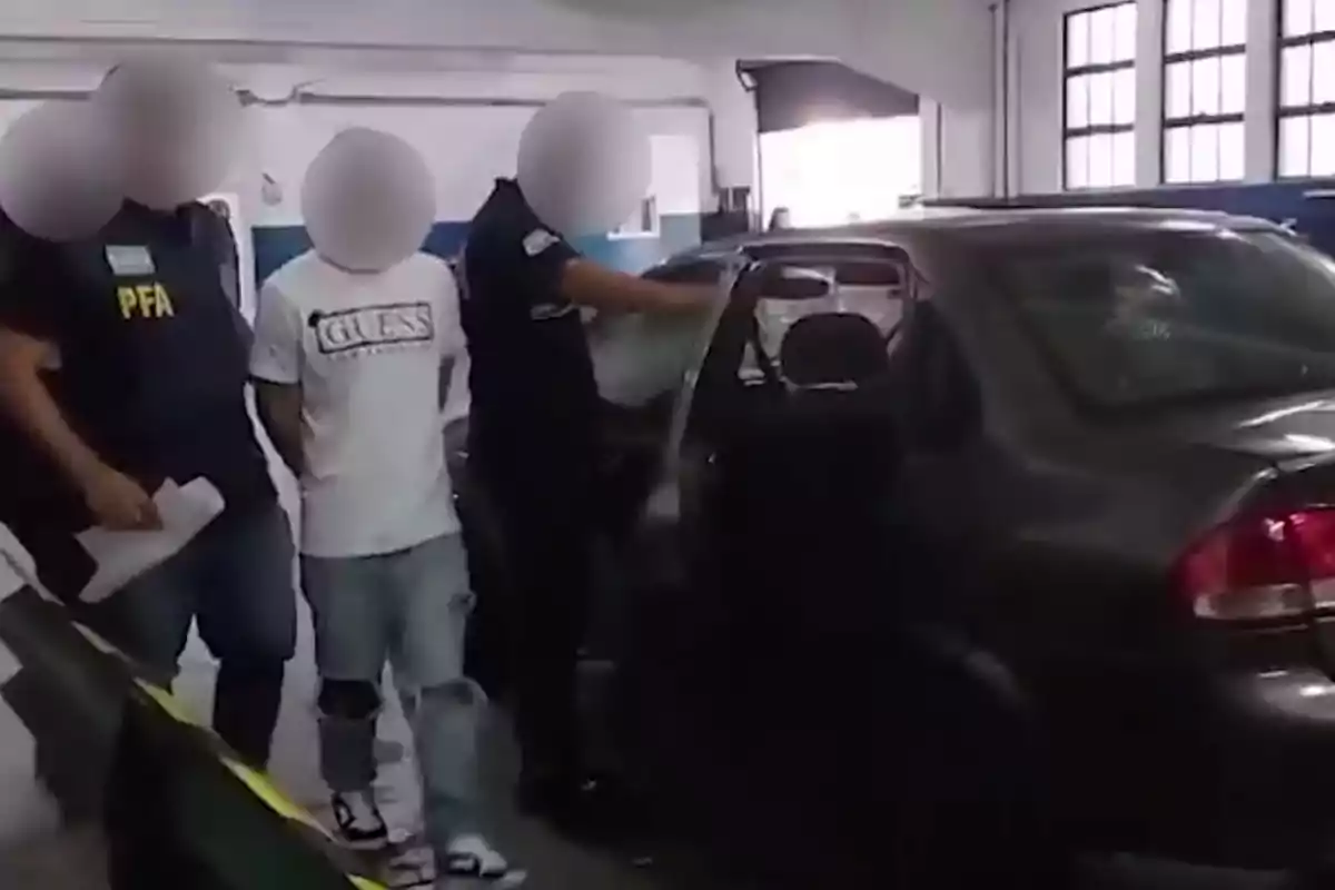 Three people with blurred faces are next to a car inside a building; one of them is wearing a white t-jersey and the other two appear to be police officers. Three people with blurred faces are next to a car inside a building; one of them is wearing a white t-jersey and the other two appear to be police officers.