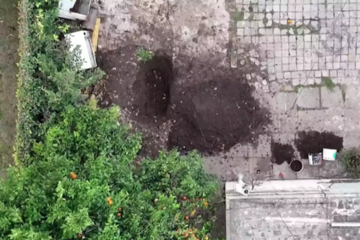 Vista aérea de un patio con tierra removida y un hoyo en el suelo junto a árboles y algunos objetos esparcidos Vista aérea de un patio con tierra removida y un hoyo en el suelo junto a árboles y algunos objetos esparcidos