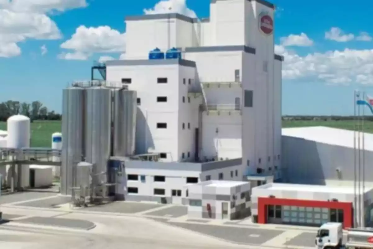 Fábrica industrial moderna con tanques de acero y camiones en el exterior bajo un cielo azul con nubes Fábrica industrial moderna con tanques de acero y camiones en el exterior bajo un cielo azul con nubes