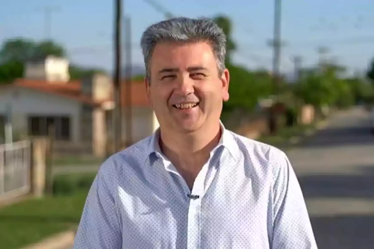 Hombre de cabello canoso y camisa clara sonriendo al aire libre en una calle residencial Hombre de cabello canoso y camisa clara sonriendo al aire libre en una calle residencial