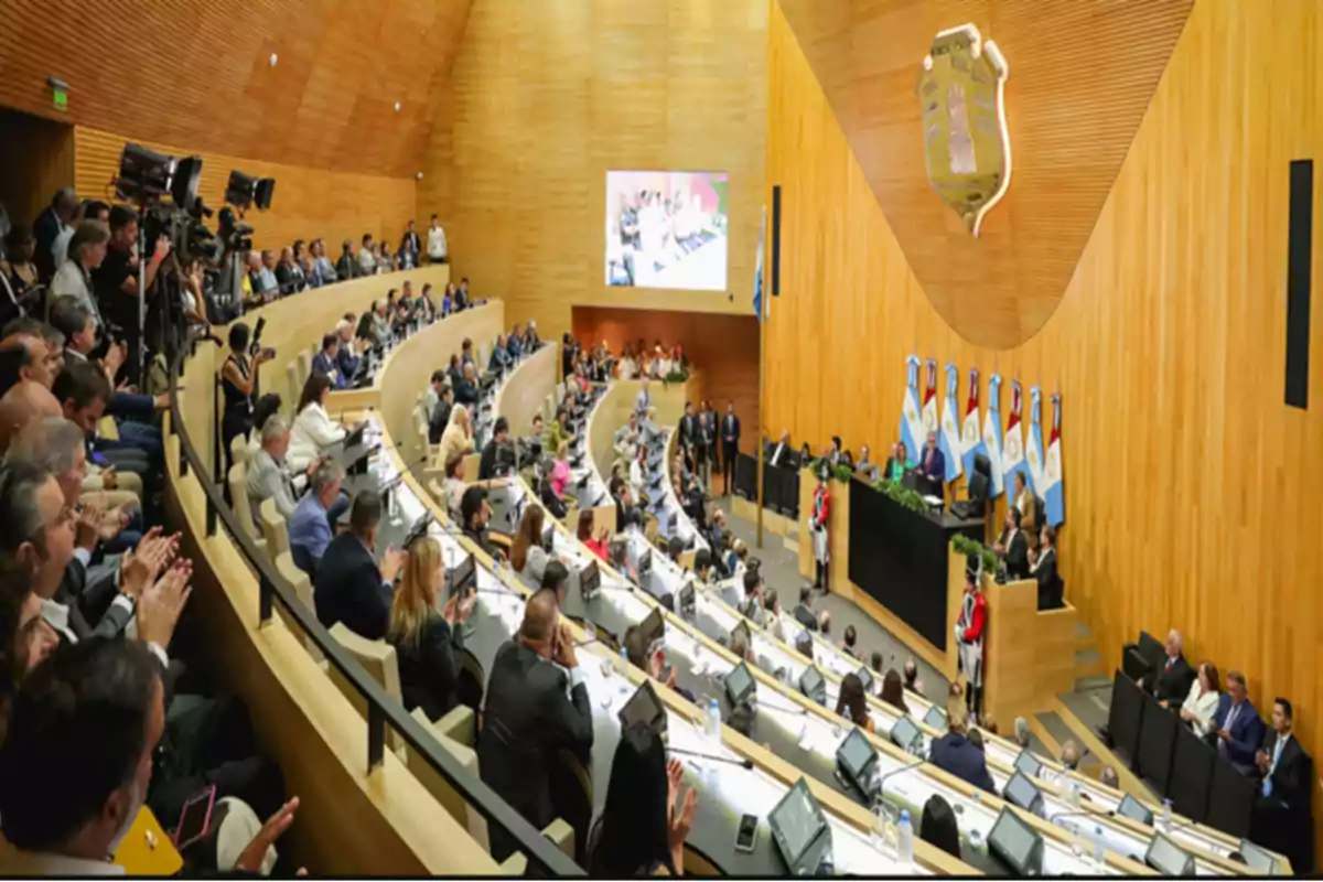 Personas reunidas en un recinto legislativo moderno con paredes de madera y banderas argentinas al fondo Personas reunidas en un recinto legislativo moderno con paredes de madera y banderas argentinas al fondo