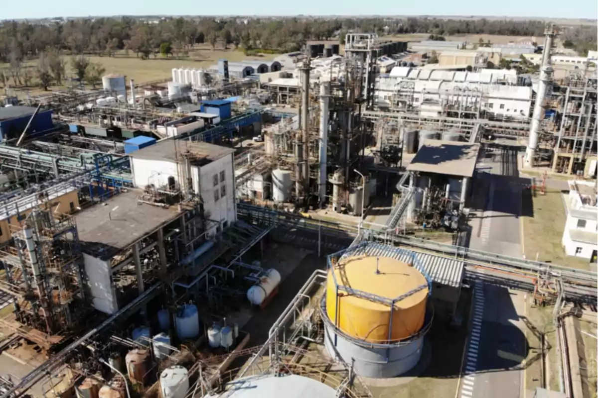 Vista aérea de una planta industrial con tanques de almacenamiento, tuberías y estructuras metálicas rodeadas de áreas verdes. Vista aérea de una planta industrial con tanques de almacenamiento, tuberías y estructuras metálicas rodeadas de áreas verdes.