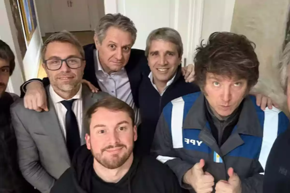 Group of six men posing together for a selfie indoors, one of them wearing a jacket with the YPF logo and giving a thumbs-up gesture