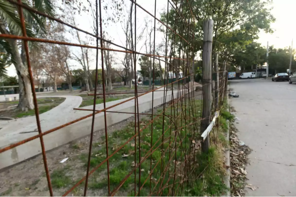 Cerca de alambre oxidado junto a una vereda en una calle arbolada Cerca de alambre oxidado junto a una vereda en una calle arbolada