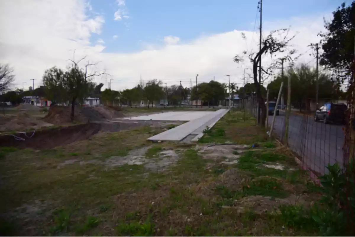 Terreno con una losa de concreto en construcción junto a una calle y árboles en un día parcialmente nublado Terreno con una losa de concreto en construcción junto a una calle y árboles en un día parcialmente nublado