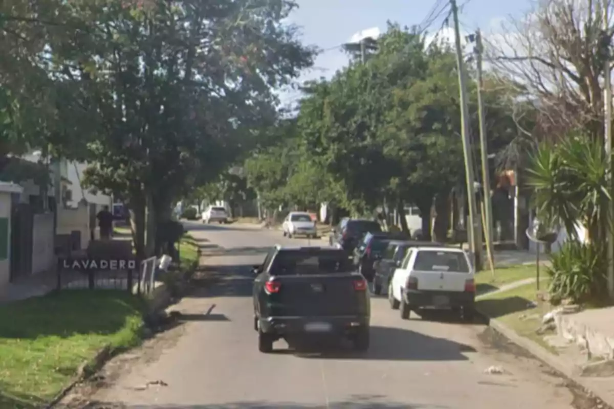 Residential street with several parked cars and trees on the sides, a sign indicates the presence of a car wash. Residential street with several parked cars and trees on the sides, a sign indicates the presence of a car wash.