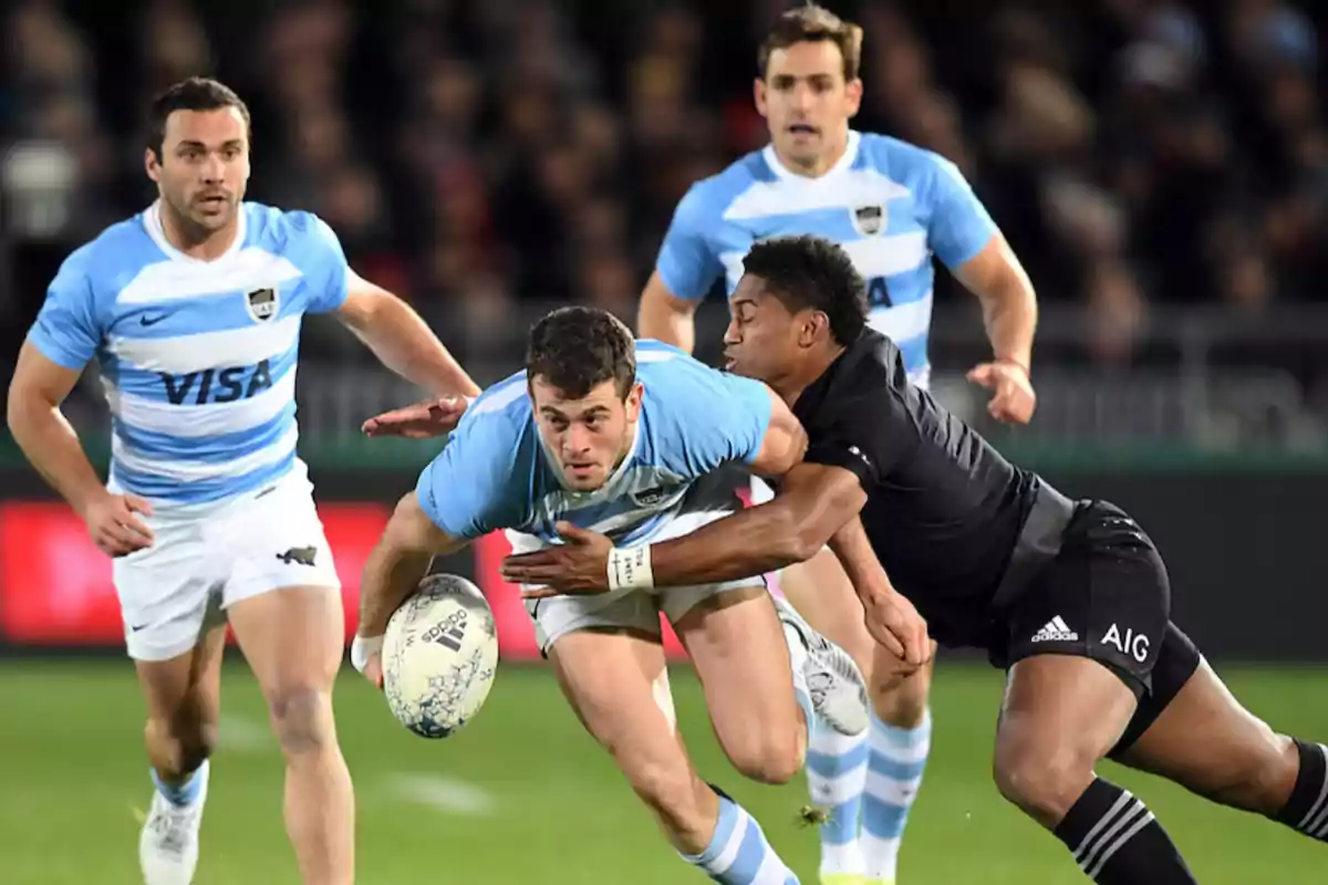 Jugador de rugby argentino intenta avanzar con el balón mientras es tackleado por un rival vestido de negro durante un partido, con otros jugadores observando la jugada en el fondo.