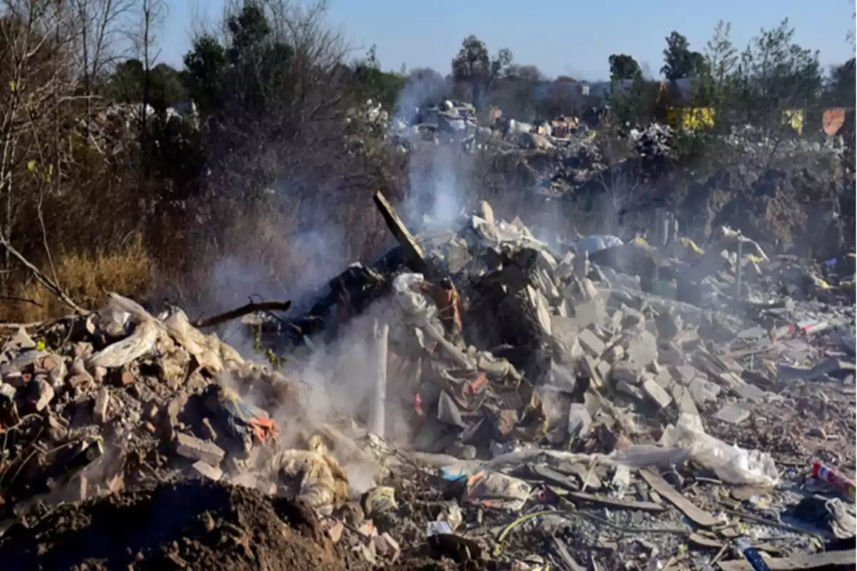 Montón de escombros y basura ardiendo en un terreno al aire libre rodeado de árboles y vegetación seca