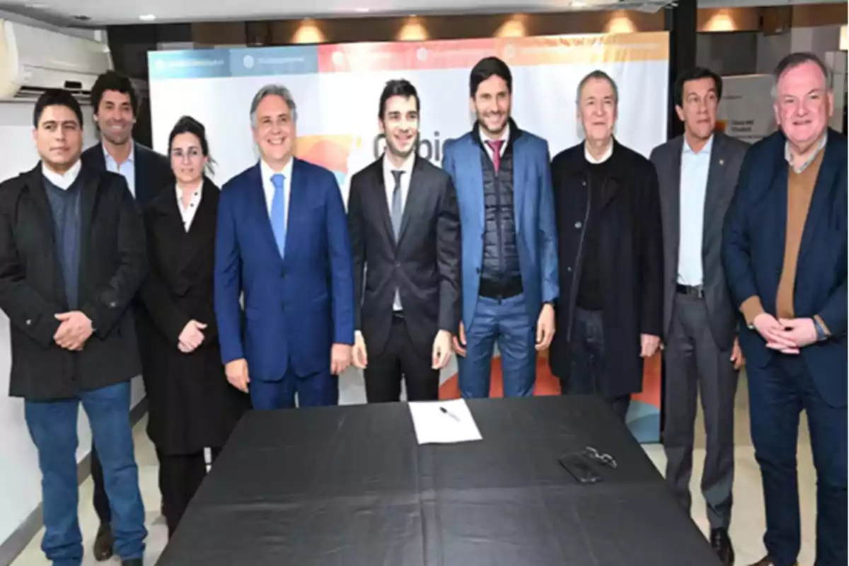 Grupo de personas vestidas formalmente posando para una foto en un evento institucional con una mesa al frente que tiene un documento y unas llaves