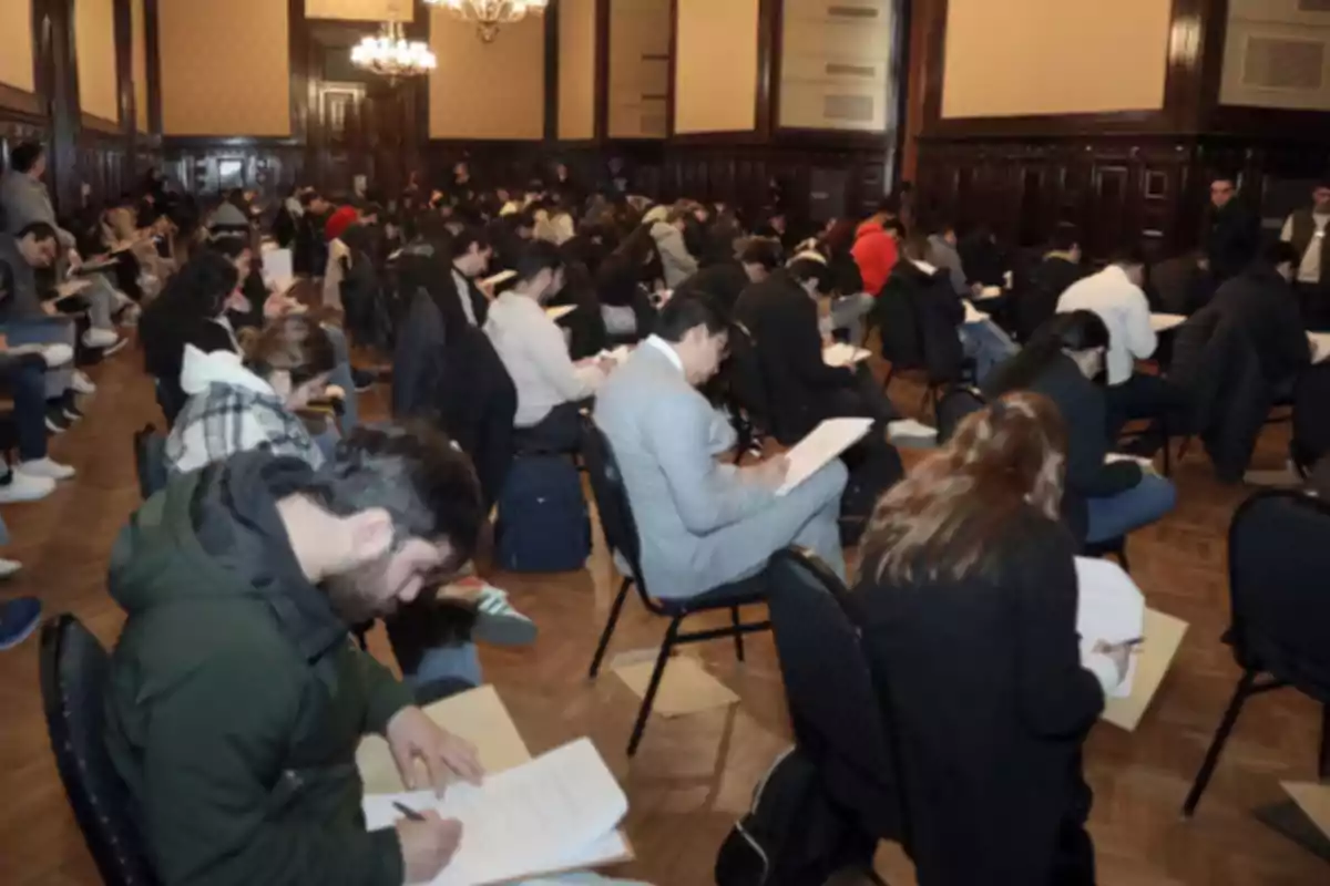 Personas sentadas en un salón grande realizando un examen escrito
