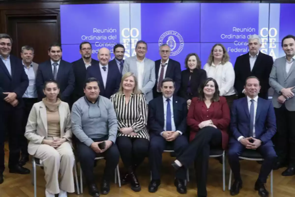 Grupo de personas posando para una foto en una sala de reuniones con pantallas de fondo que muestran el texto Reunión Ordinaria del Consejo Federal