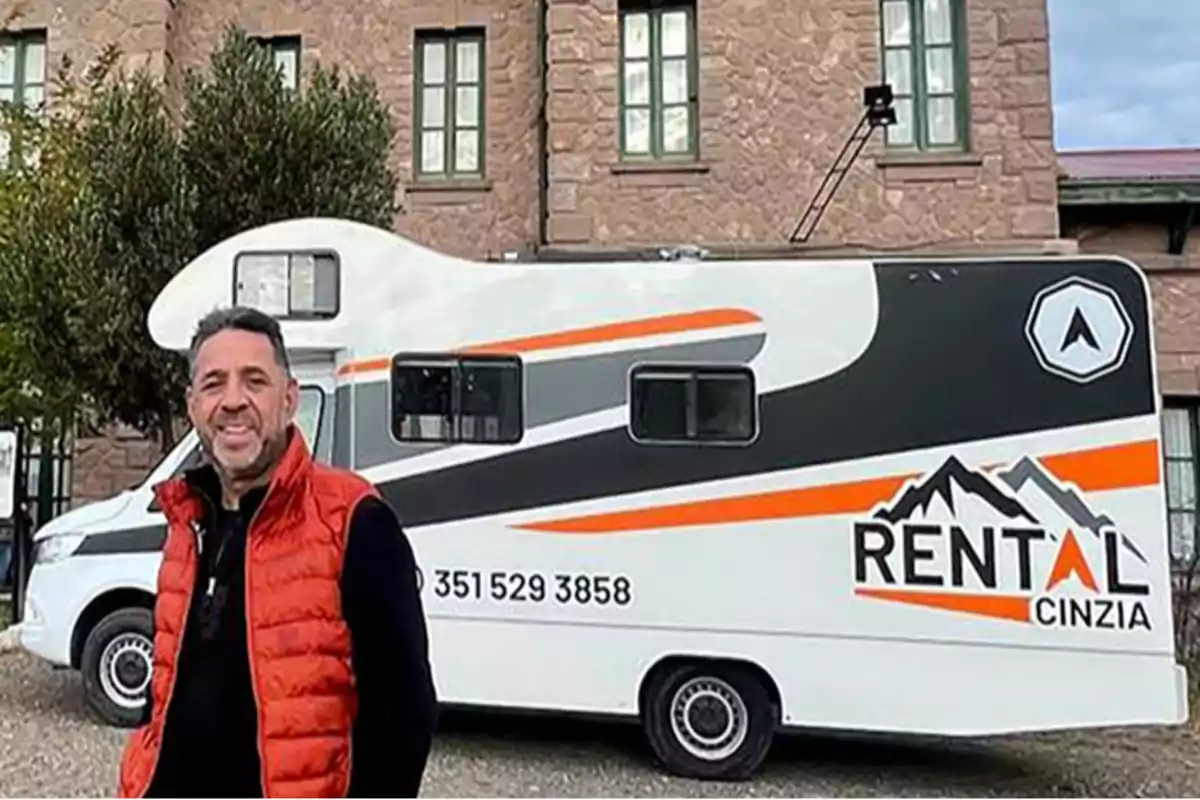 Man wearing an orange vest posing in front of a white RV with orange and black details that has a rental company logo.