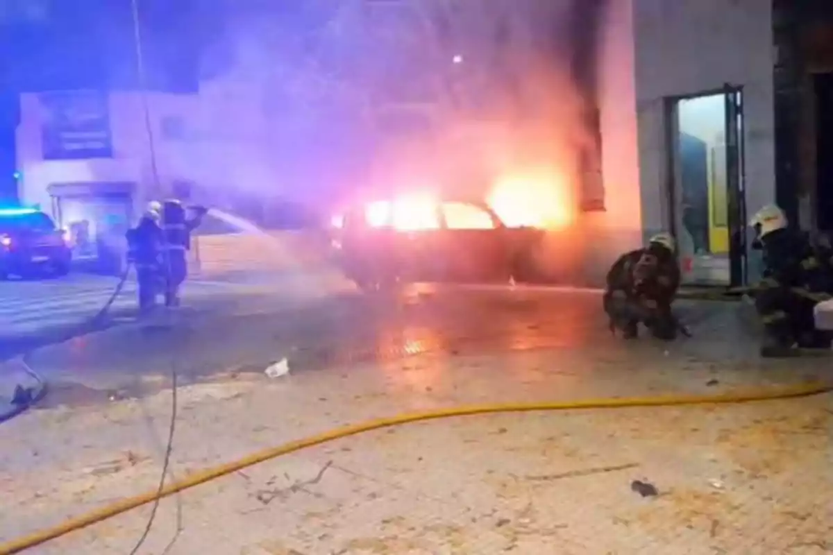 Bomberos apagan un incendio en un auto estacionado frente a un edificio durante la noche