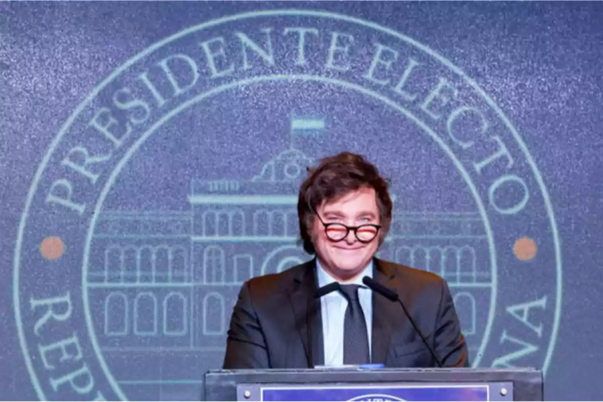 Hombre de traje y corbata hablando en un podio con un fondo que dice presidente electo y muestra un edificio institucional Hombre de traje y corbata hablando en un podio con un fondo que dice presidente electo y muestra un edificio institucional