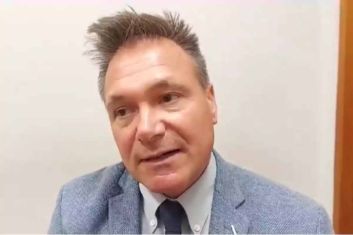 Hombre de mediana edad con saco azul claro y corbata oscura en una habitación de paredes claras Hombre de mediana edad con saco azul claro y corbata oscura en una habitación de paredes claras