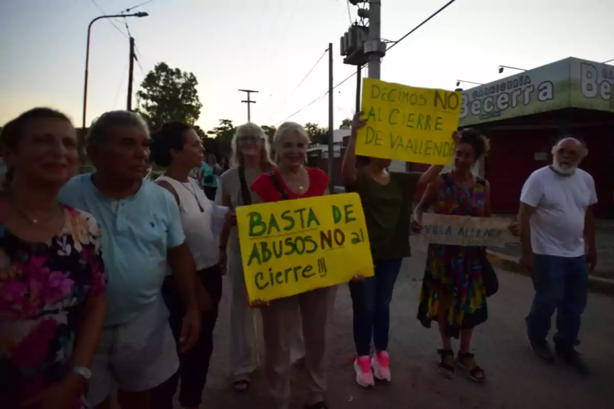 Un grupo de personas protesta en la calle sosteniendo carteles amarillos con mensajes en contra del cierre de un lugar, al fondo se ve una carnicería llamada Becerra.