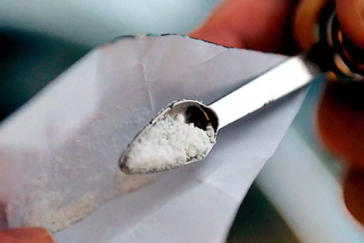 Una pequeña cuchara metálica sostiene una sustancia en polvo de color blanco sobre un papel doblado