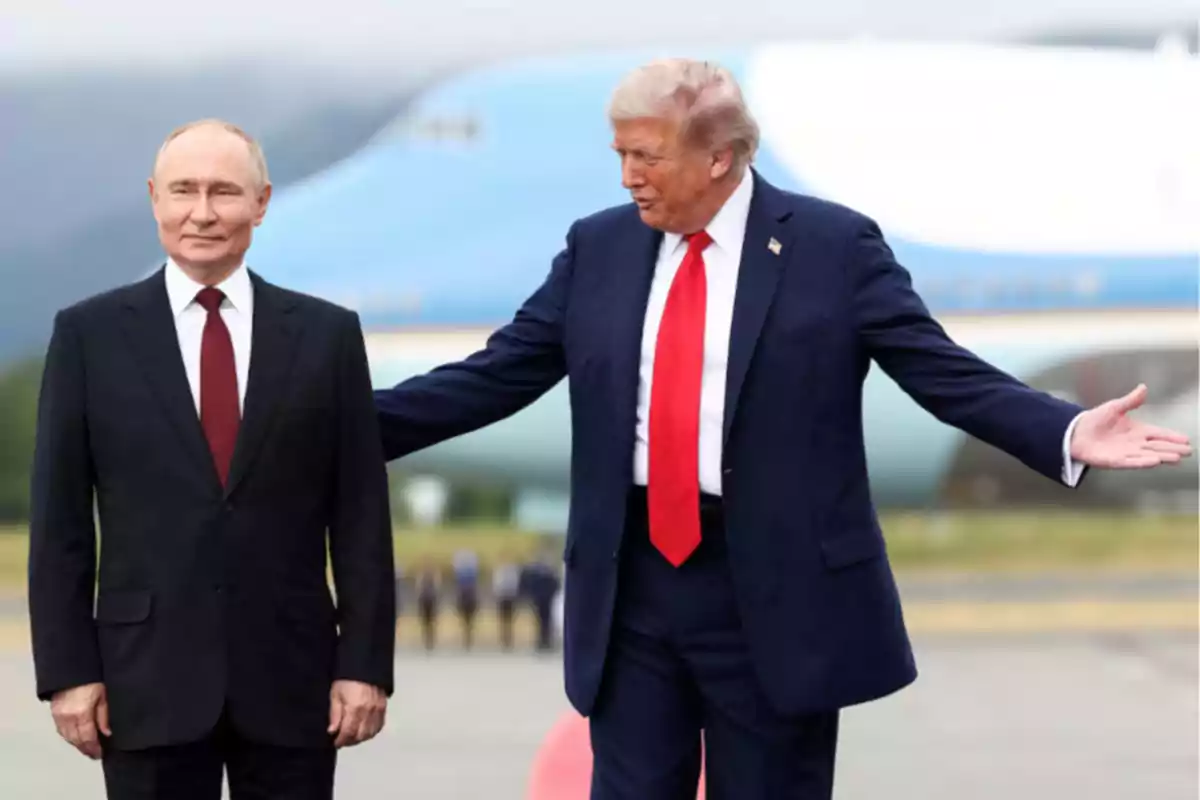 Two men in dark suits are standing on a runway with a large plane in the background; one of them is extending his arm toward the other. Two men in dark suits are standing on a runway with a large plane in the background; one of them is extending his arm toward the other.