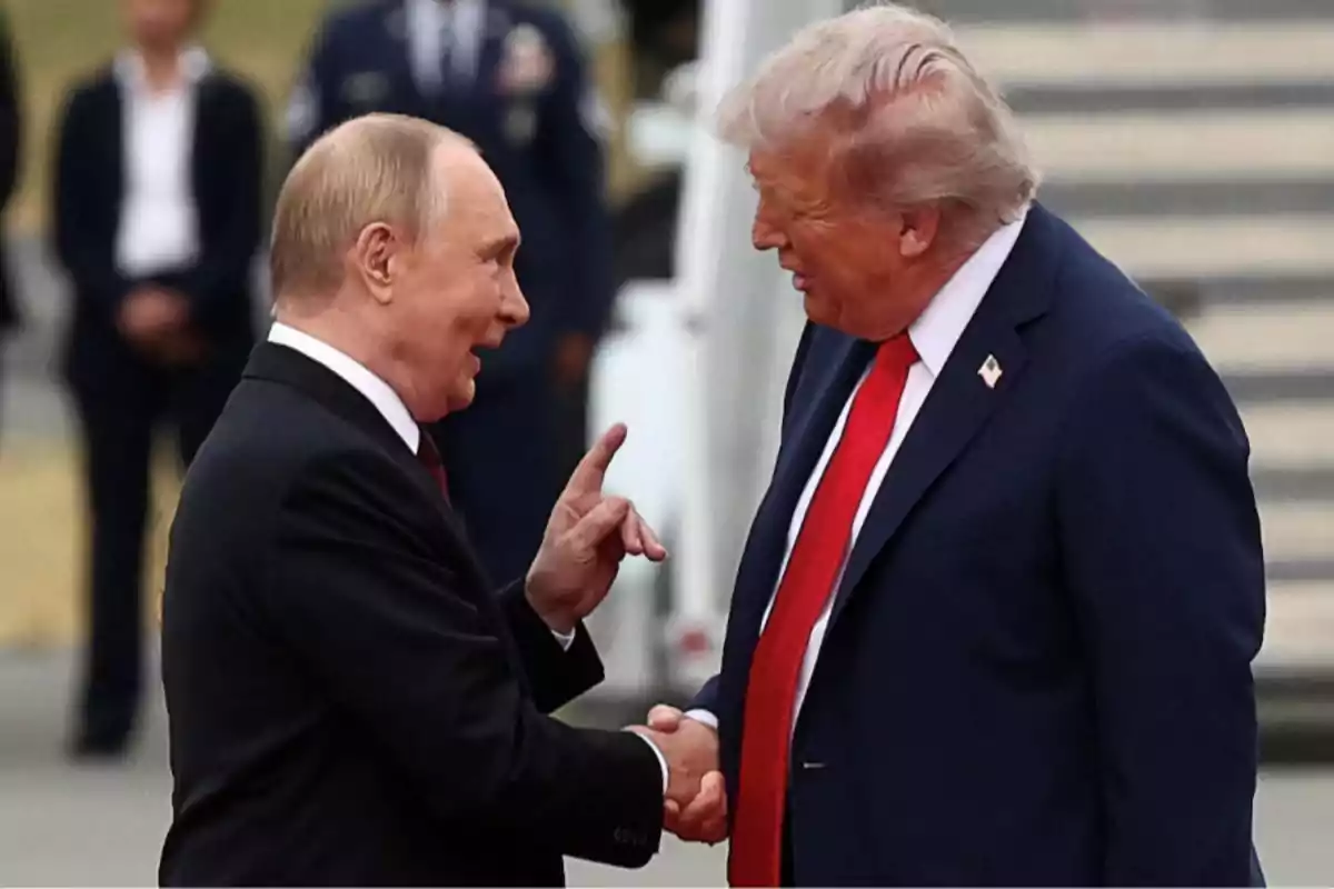 Two men in suits greet each other with a handshake while talking and smiling in a formal outdoor setting. Two men in suits greet each other with a handshake while talking and smiling in a formal outdoor setting.