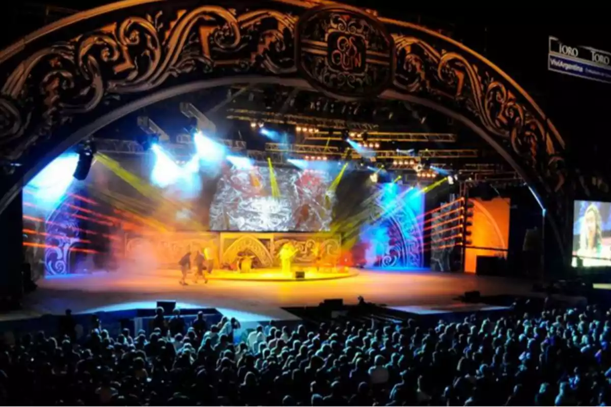 Escenario iluminado con luces de colores durante un espectáculo en un festival folclórico con público observando