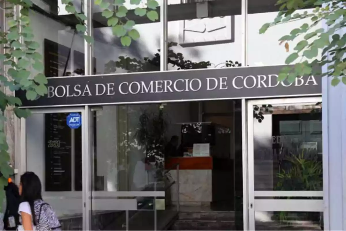 Entrada principal de la Bolsa de Comercio de Córdoba con una persona ingresando y plantas alrededor
