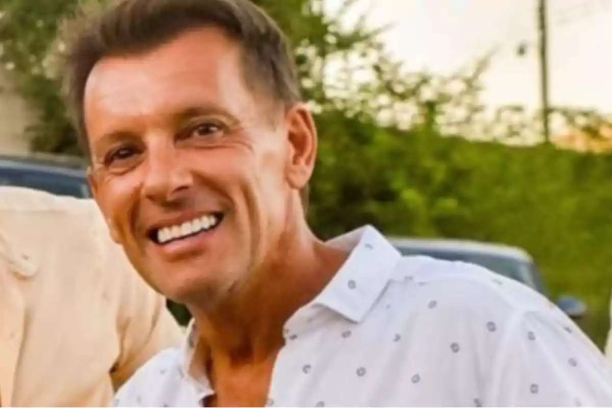 Smiling man in a white jersey with a green outdoor background