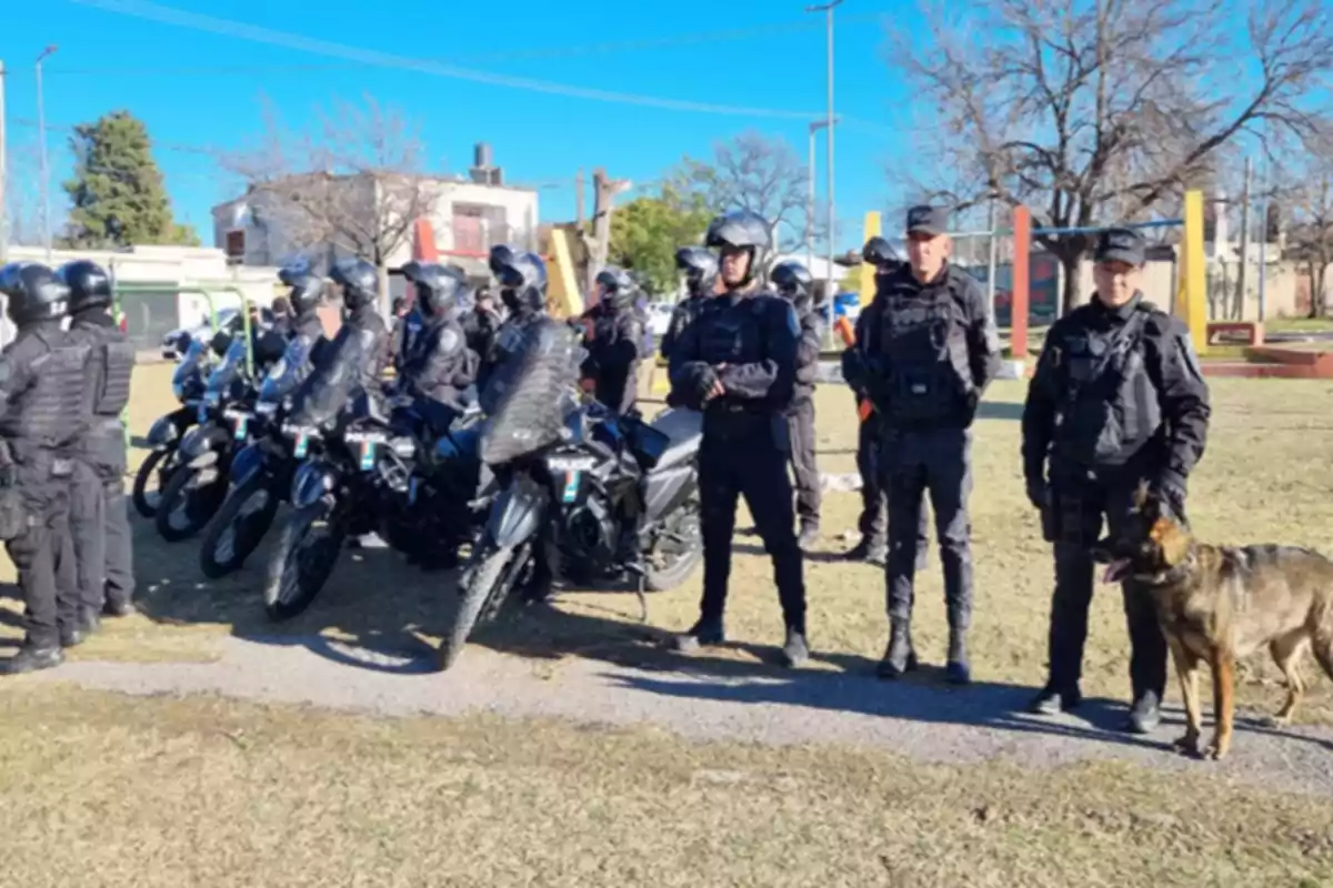 Grupo de policías con uniformes y equipo antidisturbios junto a motocicletas y un perro en un espacio al aire libre durante el día Grupo de policías con uniformes y equipo antidisturbios junto a motocicletas y un perro en un espacio al aire libre durante el día