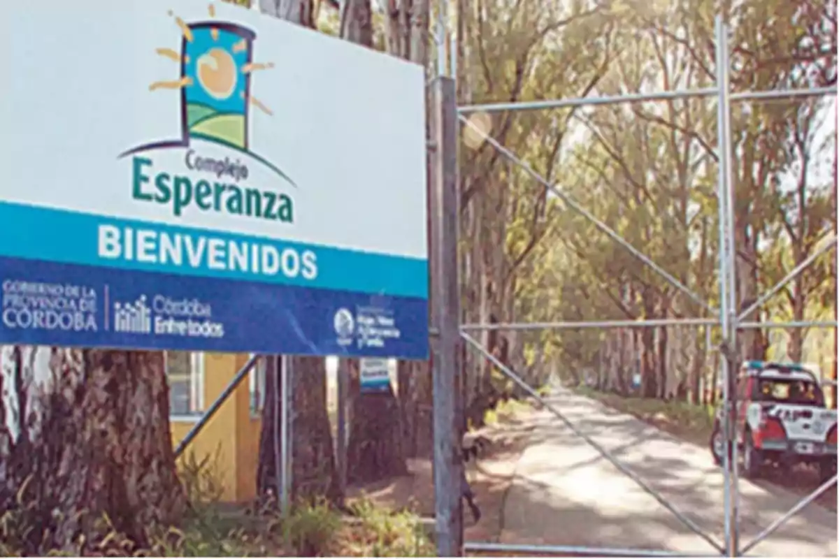 Cartel de bienvenida al Complejo Esperanza junto a un portón de entrada y una camioneta estacionada en un camino rodeado de árboles