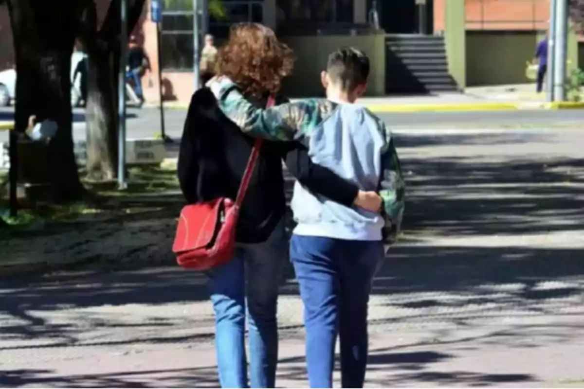 Dos personas caminando abrazadas por la calle, una lleva una bolsa roja y ambas están de espaldas