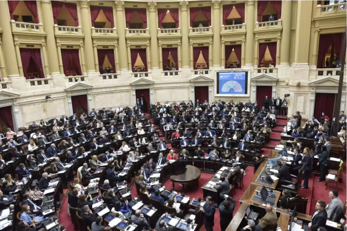 Vista panorámica de una sesión parlamentaria en un recinto legislativo con numerosos diputados sentados en sus bancas y público en los palcos Vista panorámica de una sesión parlamentaria en un recinto legislativo con numerosos diputados sentados en sus bancas y público en los palcos