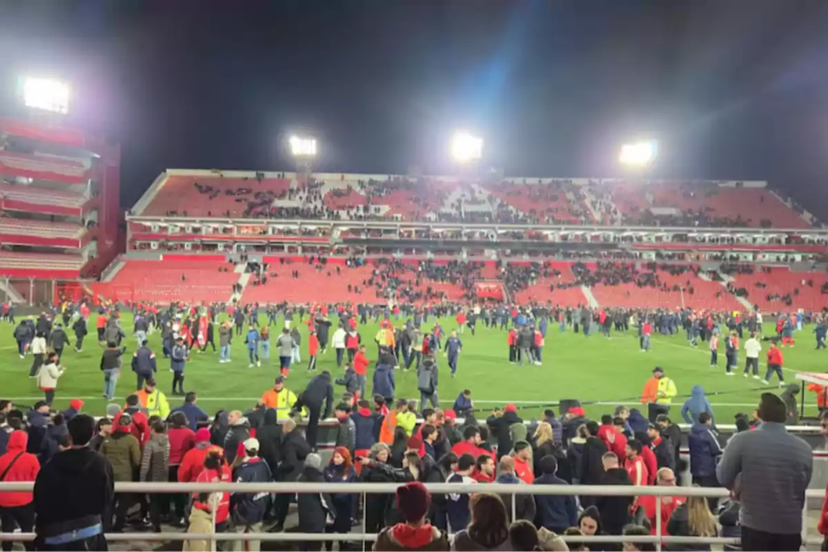 People invading the field of a soccer stadium at night with the stands partially occupied and the lights on People invading the field of a soccer stadium at night with the stands partially occupied and the lights on