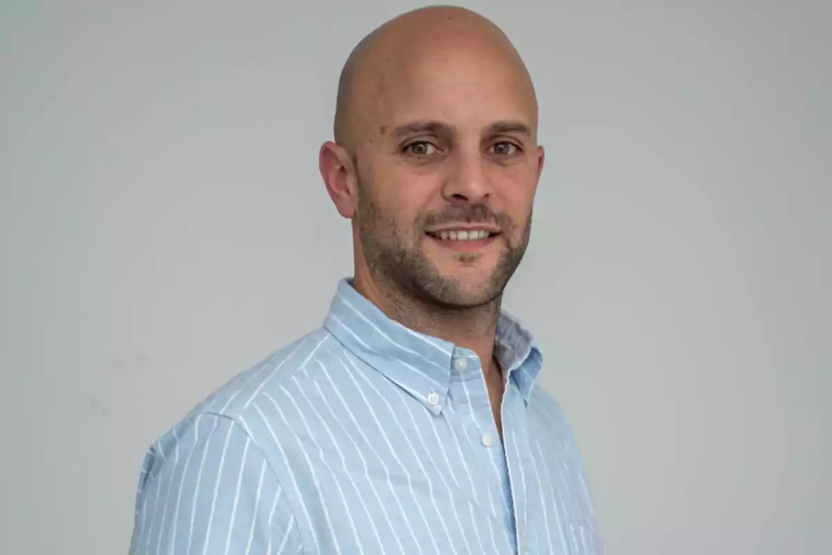 Bald man with a short beard and a blue striped jersey posing and smiling in front of a light gray background Bald man with a short beard and a blue striped jersey posing and smiling in front of a light gray background