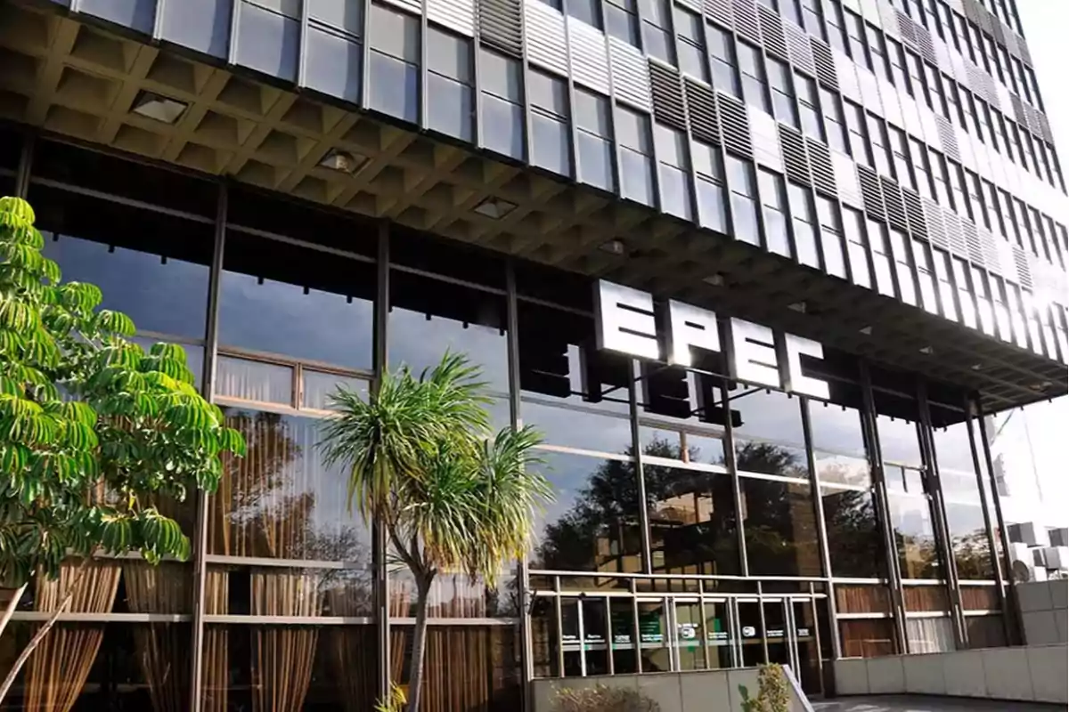 Facade of a modern building with large windows and the illuminated EPEC sign at the entrance, surrounded by plants and trees Facade of a modern building with large windows and the illuminated EPEC sign at the entrance, surrounded by plants and trees